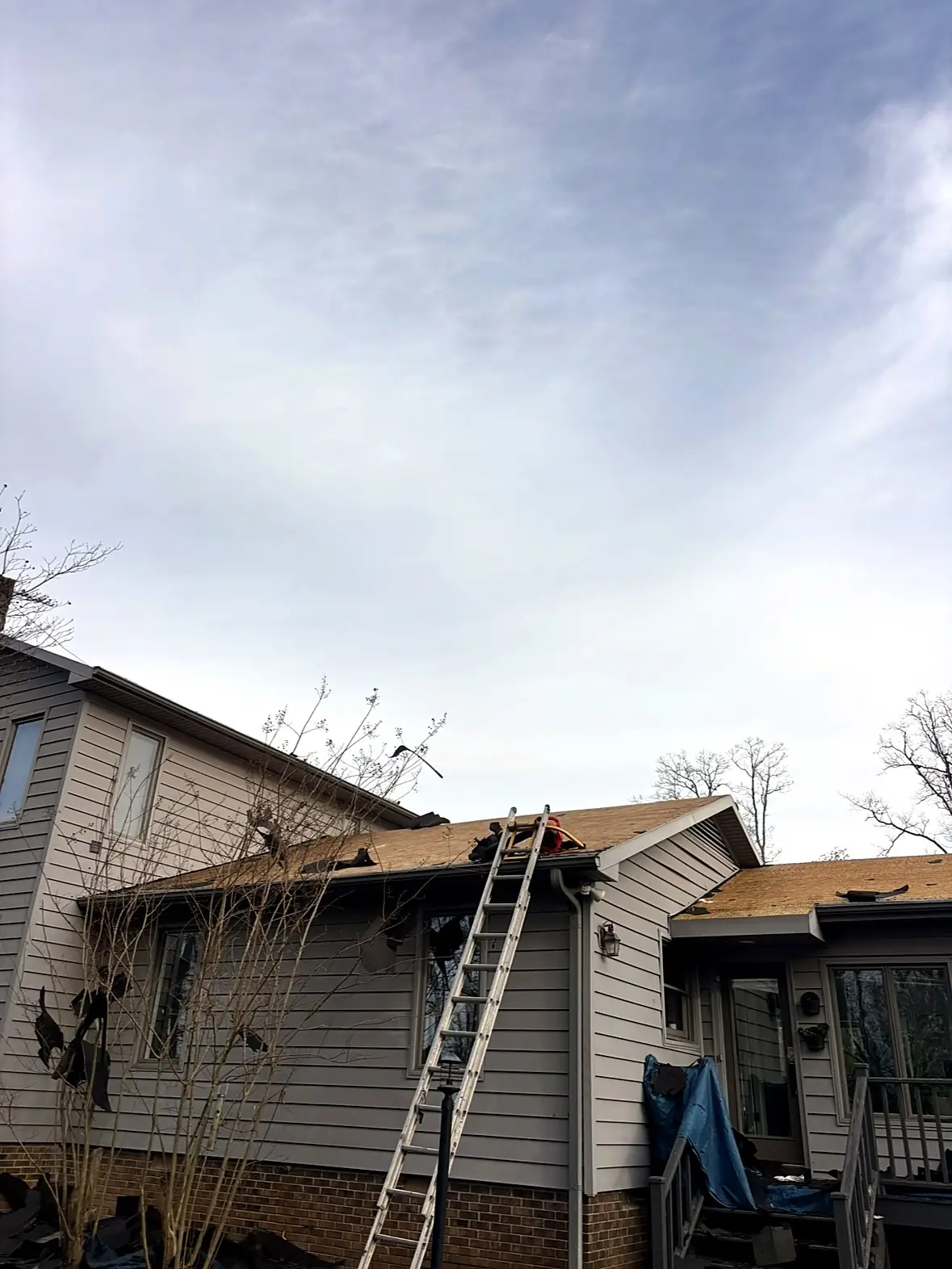 Roofing crew tearing off an old shingle roof on a two-story house, ladder against the gutter, Kings Mountain NC